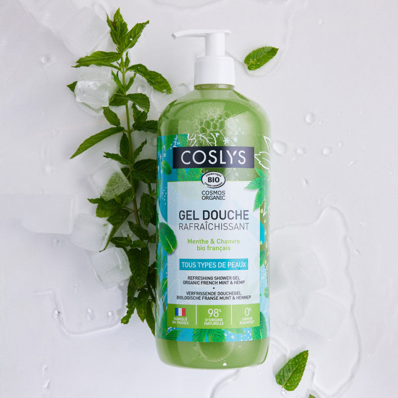 Gel de ducha verde Coslys Menta y Cáñamo con dosificador sobre un fondo con hojas de menta
