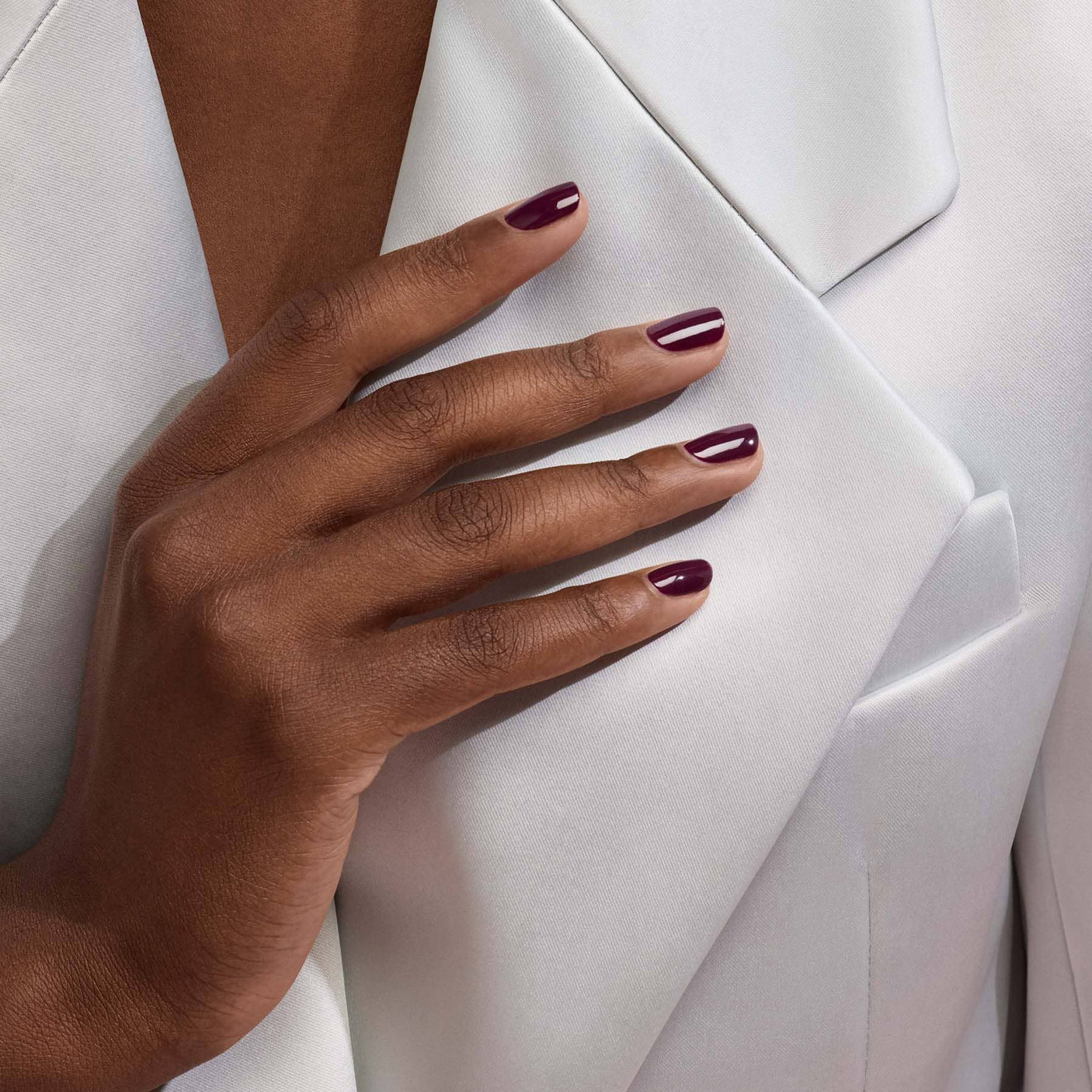 Look de invierno con el esmalte Ciruela de Manucurist: contraste elegante entre las uñas oscuras y un abrigo blanco.