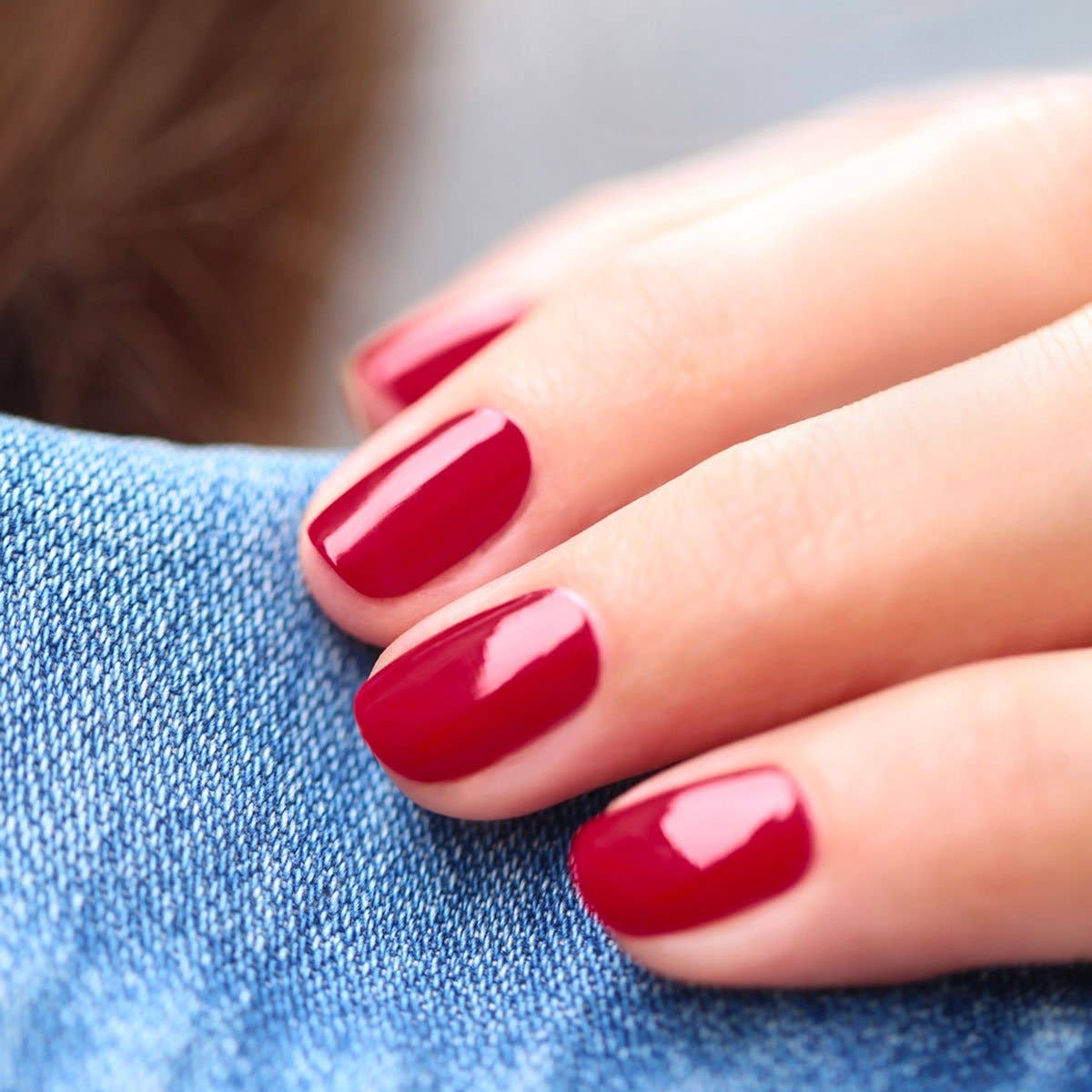 Manos con uñas cortas pintadas en color Granada de Manucurist, un rojo clásico elegante y luminoso.