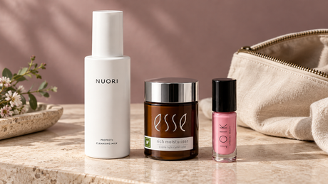 Leche limpiadora NUORI, crema Esse y aceite labial JOIK junto a un neceser: composición editorial de Oportunidades Biovardi creada con IA