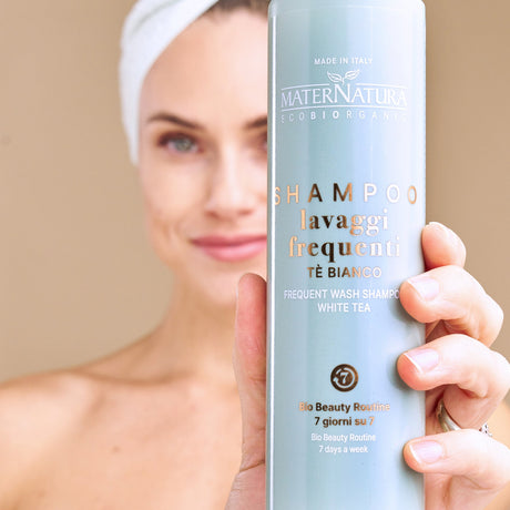 Modelo con una toalla en el cabello mostrando la botella del champú de té blanco Maternatura