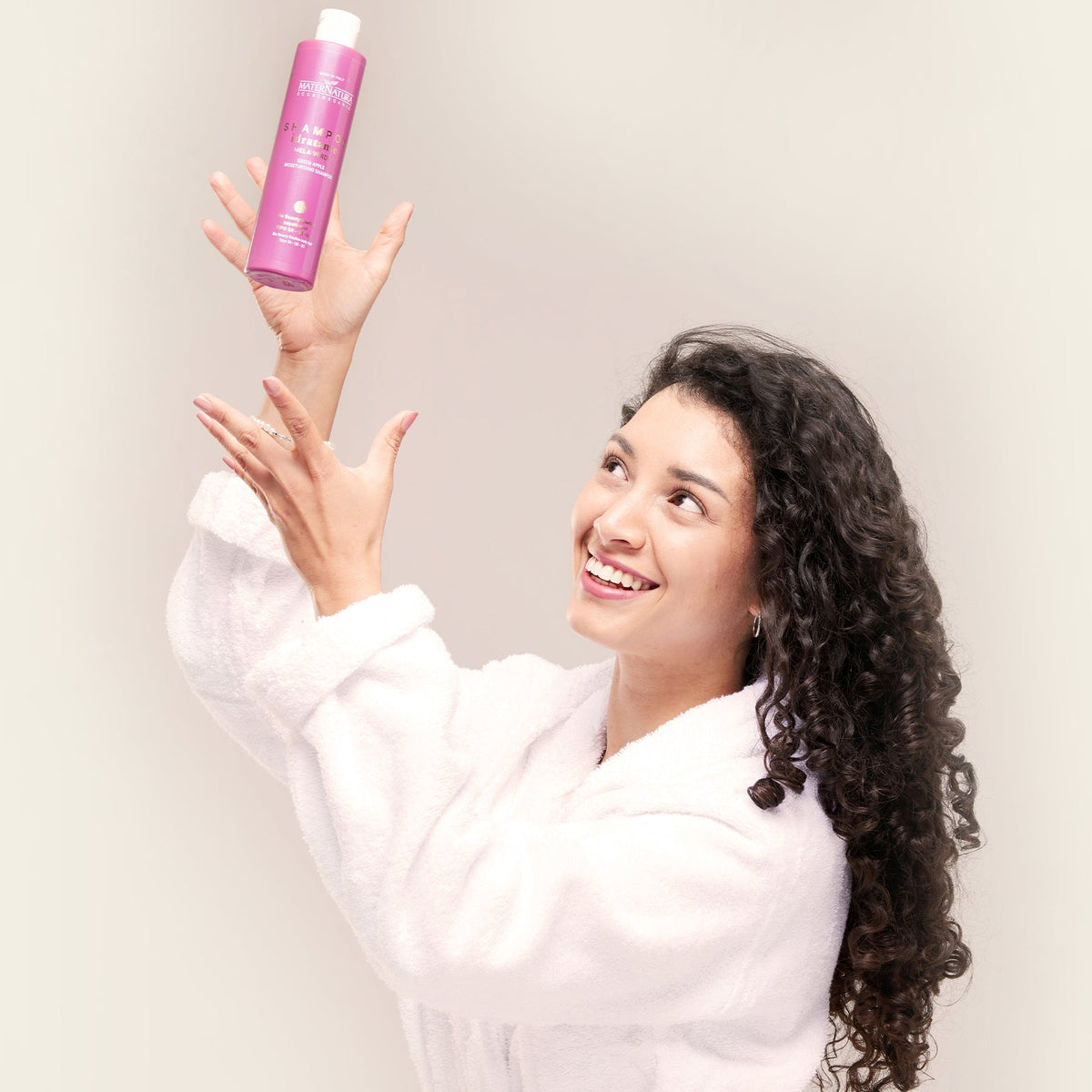 Modelo de pelo rizado mostrando la botella rosa del champú de manzana verde Maternatura