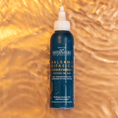 Envase azul del acondicionador bifásico con proteínas de arroz Maternatura sobre un fondo dorado