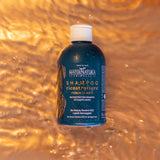 Botella azul del champú reconstructor Maternatura con hojas de mate sobre un fondo dorado