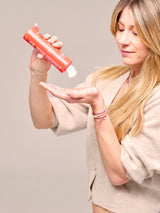 Modelo vertiendo champú de aguacate Maternatura desde la botella coral sobre la palma