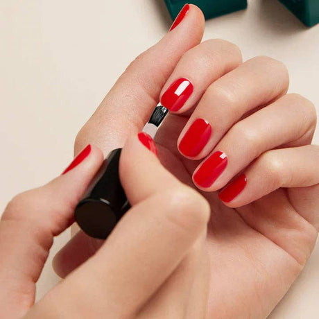 Aplicación del Top Coat Sunshine sobre el esmalte de uñas para sellar el color y activar el brillo con luz natural.