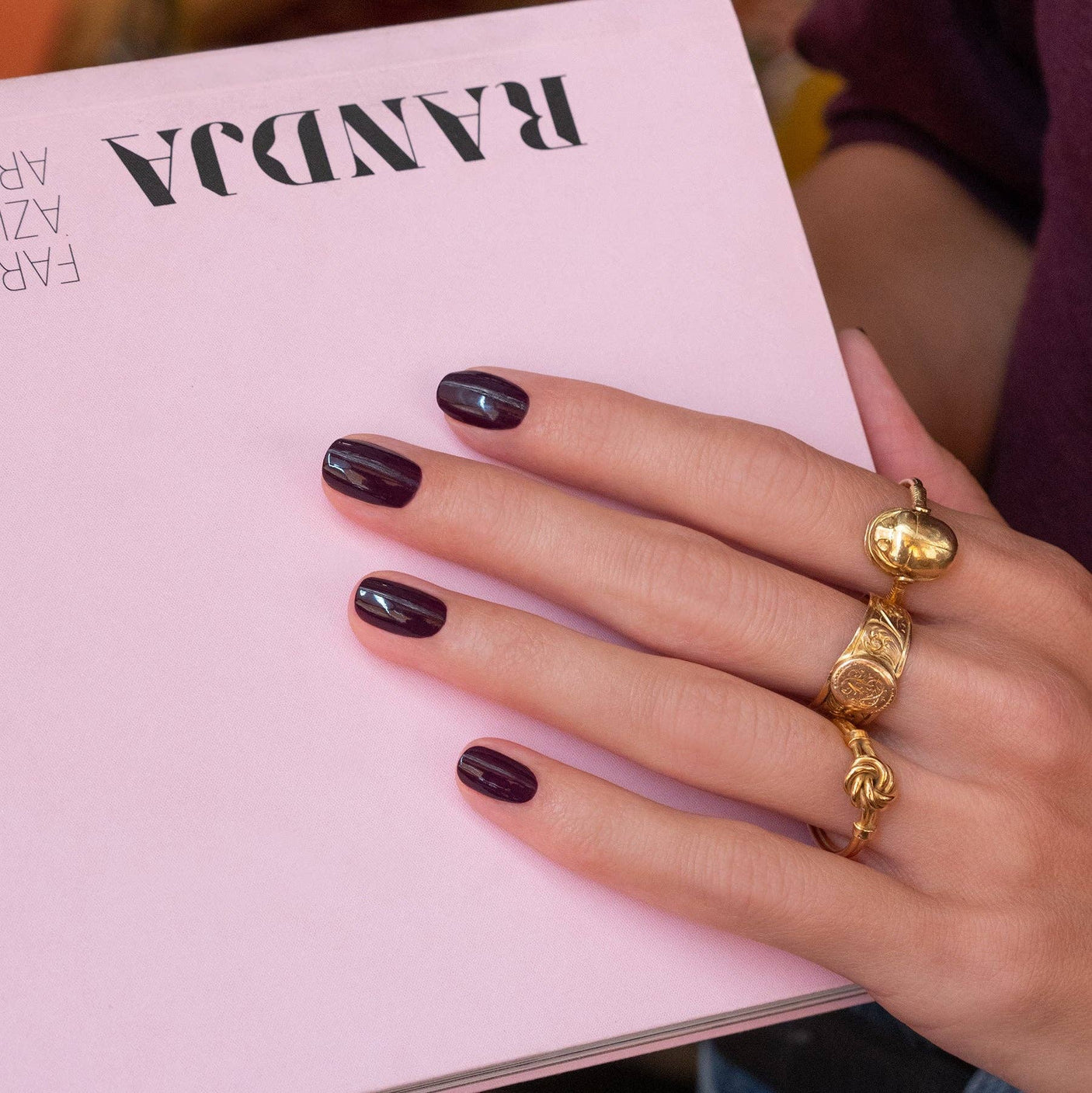 Manos con uñas pintadas en tono Berenjena de Manucurist sosteniendo un libro, un look de otoño sofisticado y natural.