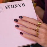 Manos con uñas pintadas en tono Berenjena de Manucurist sosteniendo un libro, un look de otoño sofisticado y natural.