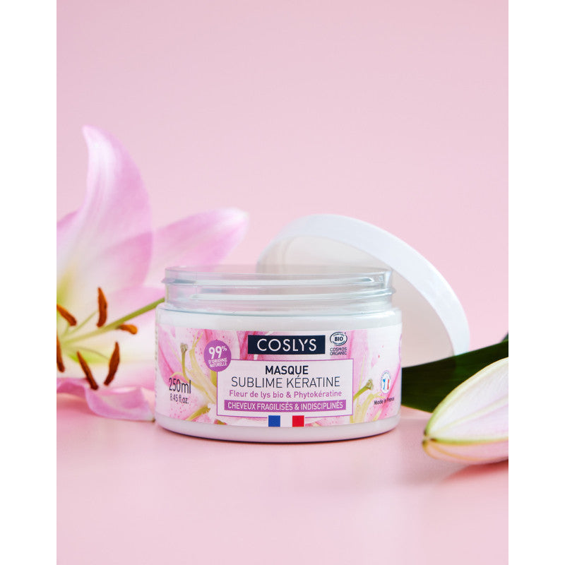 Tarro abierto de mascarilla Sublime Keratina Coslys de 250 ml junto a flores sobre un fondo rosa