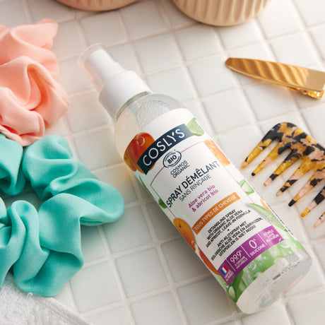 Spray desenredante Coslys con aloe vera y albaricoque junto a coleteros y un peine