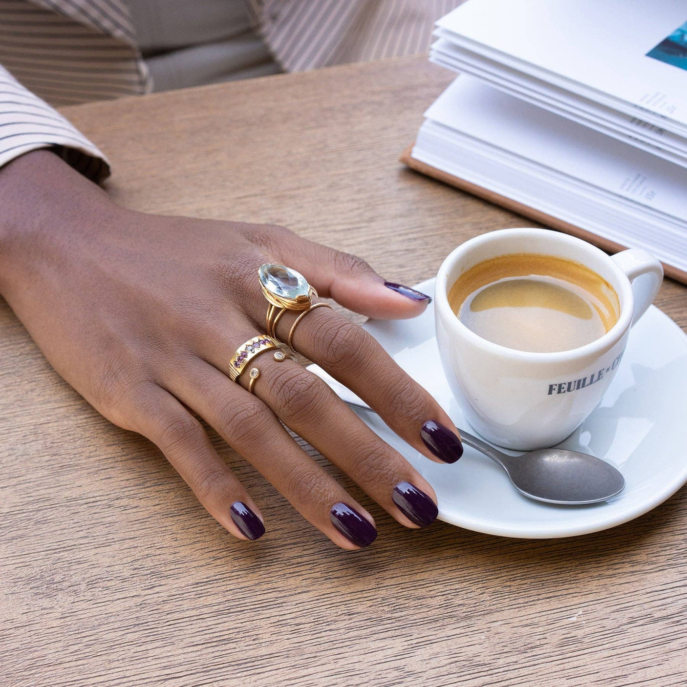 Primer plano de una manicura morada oscura con el color Berenjena de Manucurist sujetando una taza de café caliente en Biovardi.